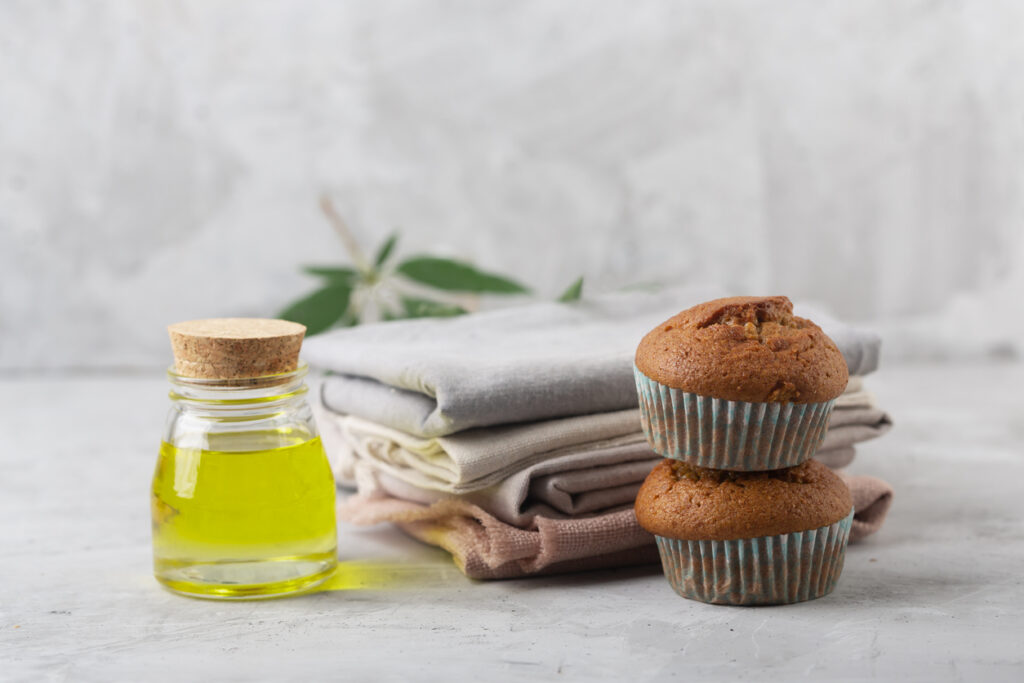 Image of CBD oil and muffins, with hemp cloth behind them and an out of focus hemp leaf behind that, in an overall neutral environment.